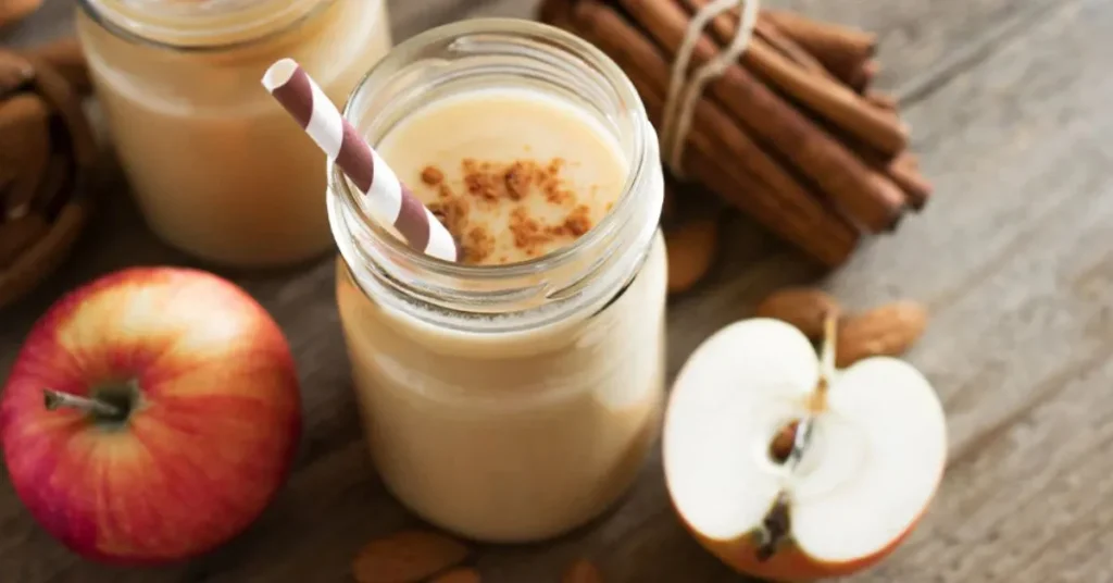 A creamy apple cinnamon protein smoothie in a glass, topped with a sprinkle of cinnamon and a fresh apple slice.