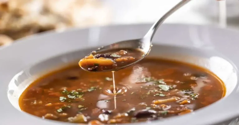 A bowl of hearty Instant Pot Minestrone Soup with fresh vegetables, beans, and pasta garnished with parsley, served on a wooden table