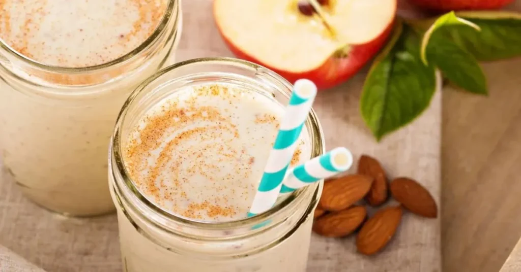 A creamy apple cinnamon protein smoothie in a glass, topped with a sprinkle of cinnamon and a fresh apple slice.