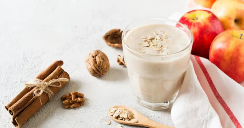 A creamy apple cinnamon protein smoothie in a glass, topped with a sprinkle of cinnamon and a fresh apple slice.