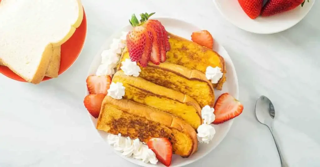 French toast slices garnished with powdered sugar, fresh fruits, and maple.