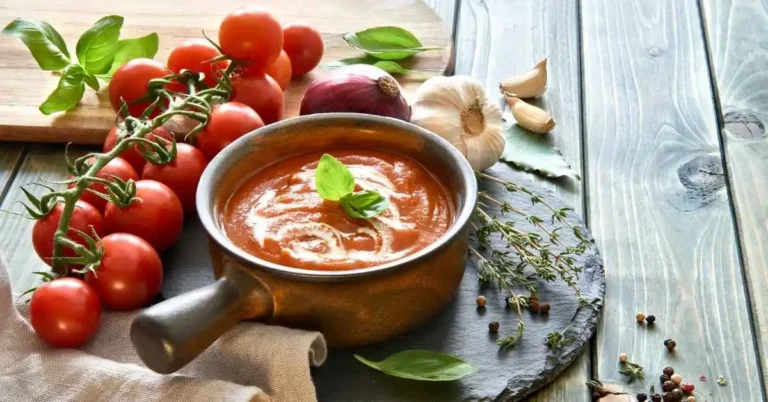 A bowl of creamy homemade fresh tomato soup garnished with fresh basil leaves.