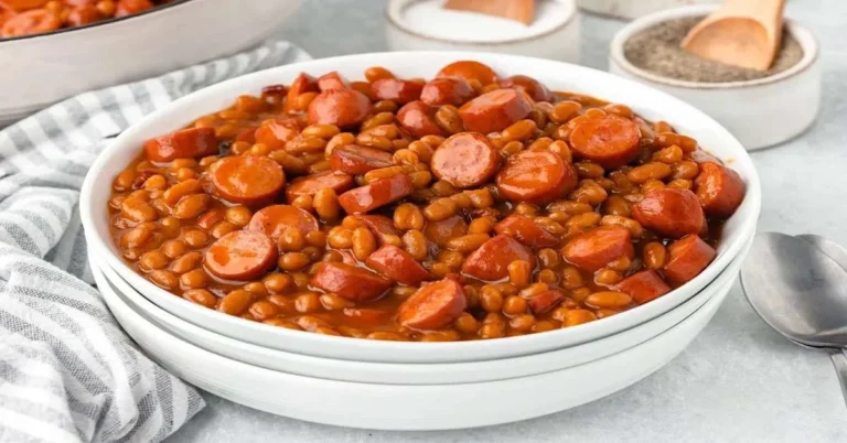 Homemade beanie weenies with sausages and baked beans served in a rustic bowl.