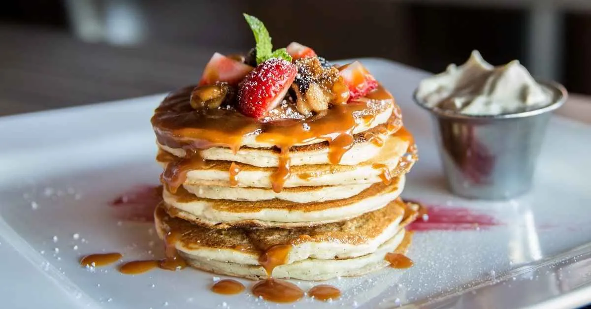 A stack of fluffy, golden-brown pancakes topped with fresh berries and drizzled with syrup.