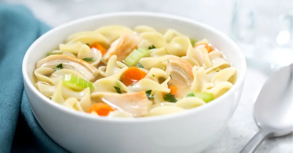 A bowl of homemade chickpea noodle soup with carrots, celery, and herbs in a flavorful broth.