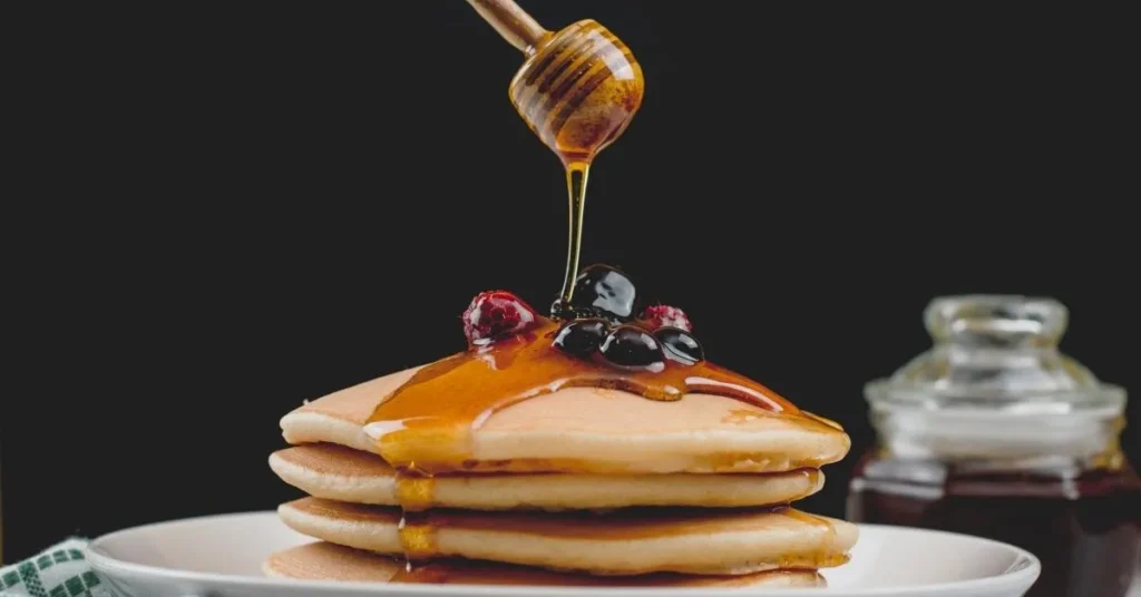 A stack of fluffy, golden-brown pancakes topped with a pat of butter and drizzled with maple syrup.