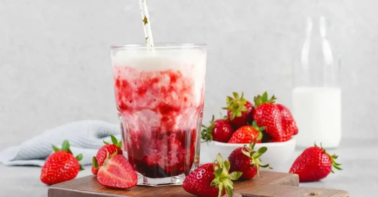 Simple strawberry smoothie in a glass with fresh strawberries and a mint garnish on a wooden table.