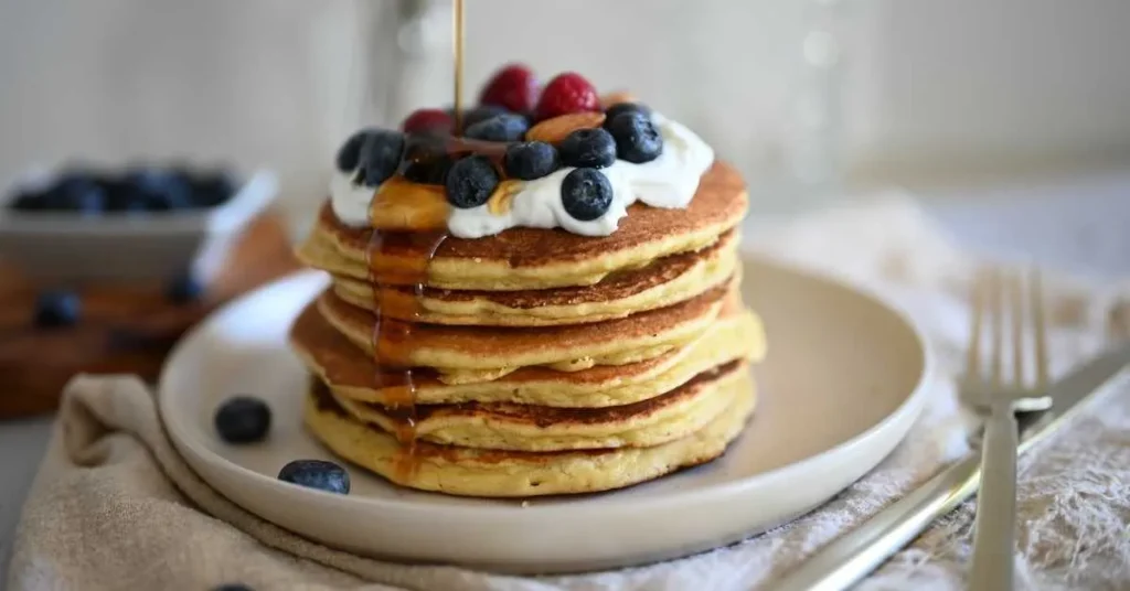 A plate of golden, fluffy pancakes stacked high, topped with butter, fresh strawberries, and maple syrup.