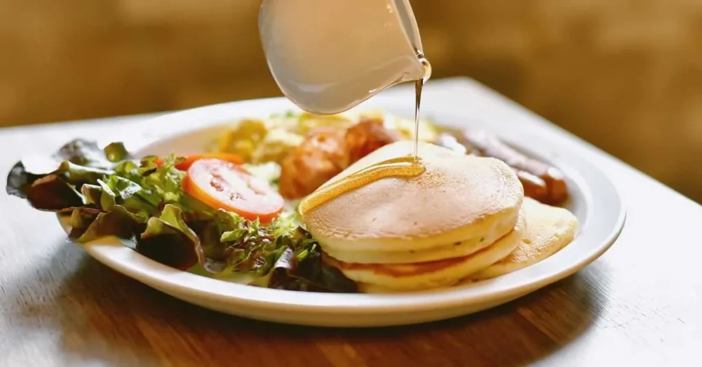 A stack of pancakes topped with fresh fruit and syrup, served on a breakfast table with juice and coffee.
