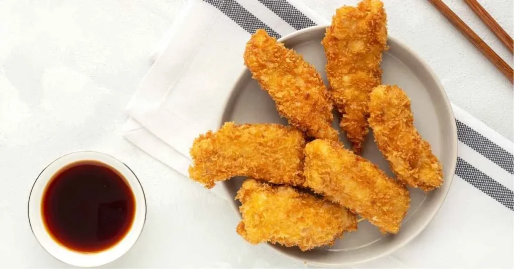 Golden-brown chicken nuggets served with dipping sauce on a plate.