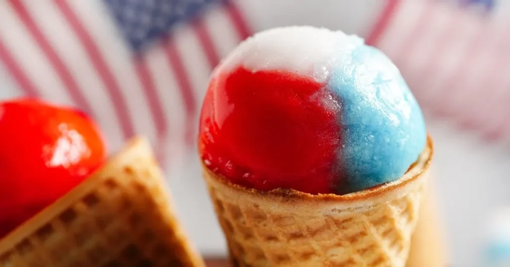 Colorful snow cones in paper cups with syrup drizzled on top.