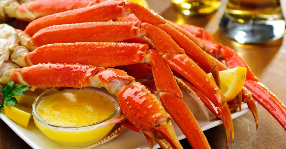 A plate of freshly cooked snow crab legs served with melted butter and lemon wedges.